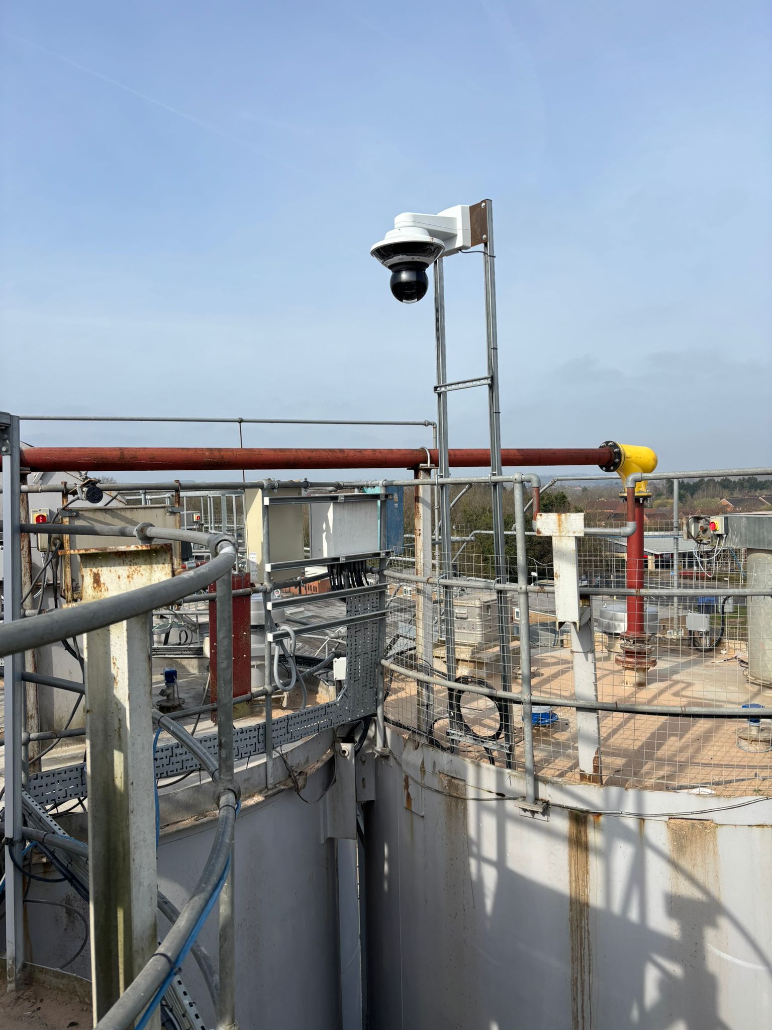 Industrial setting with a security camera on a metal platform against a blue sky.