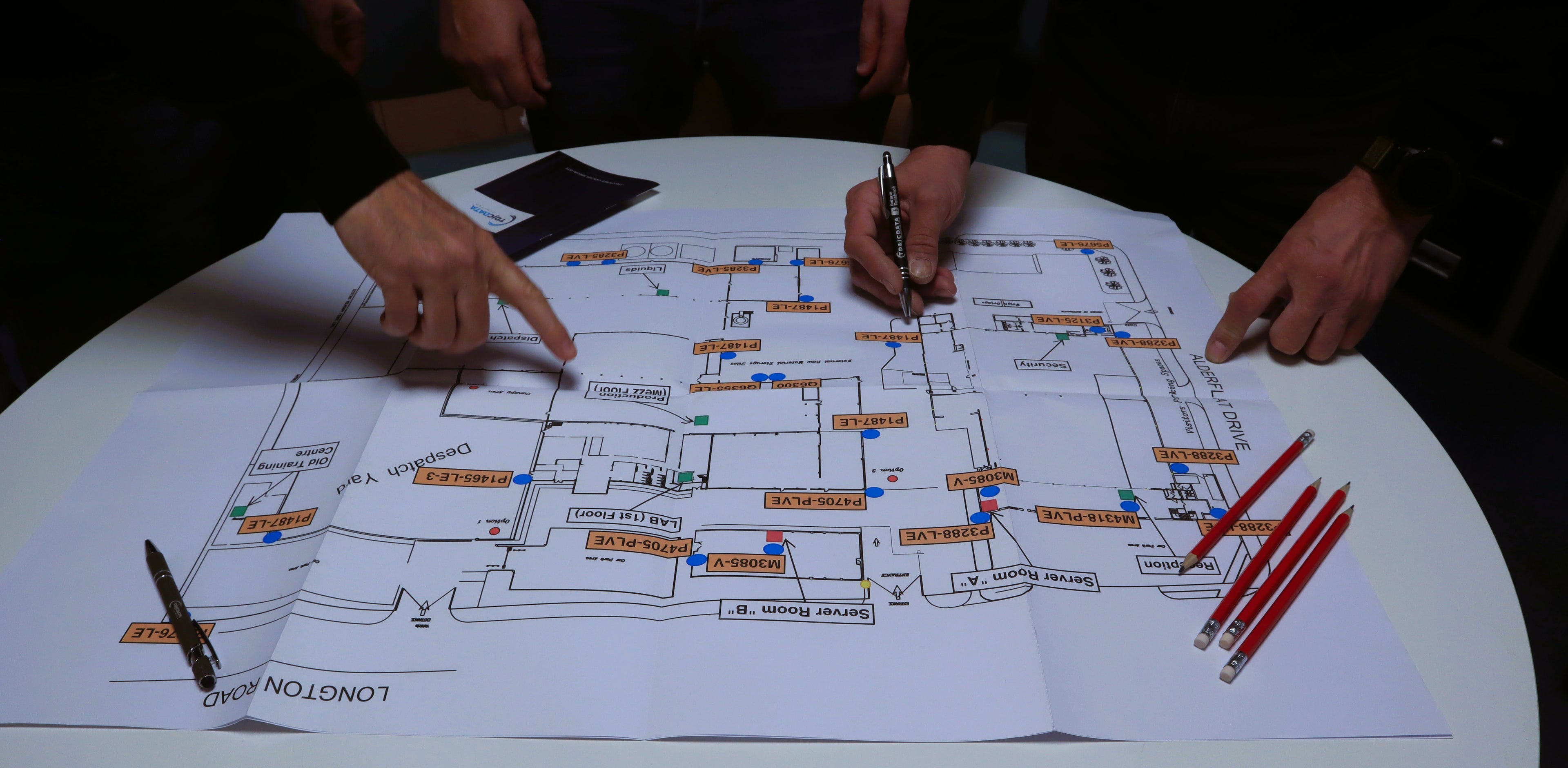 Two people working on a detailed map with markers and pencils on a table.