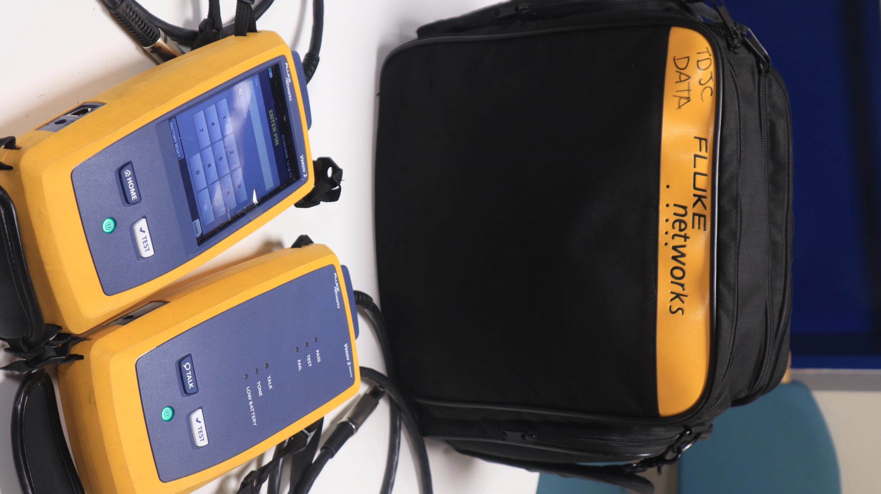 Two Fluke network testers with a black bag labeled 'Fluke Networks' on a white background.