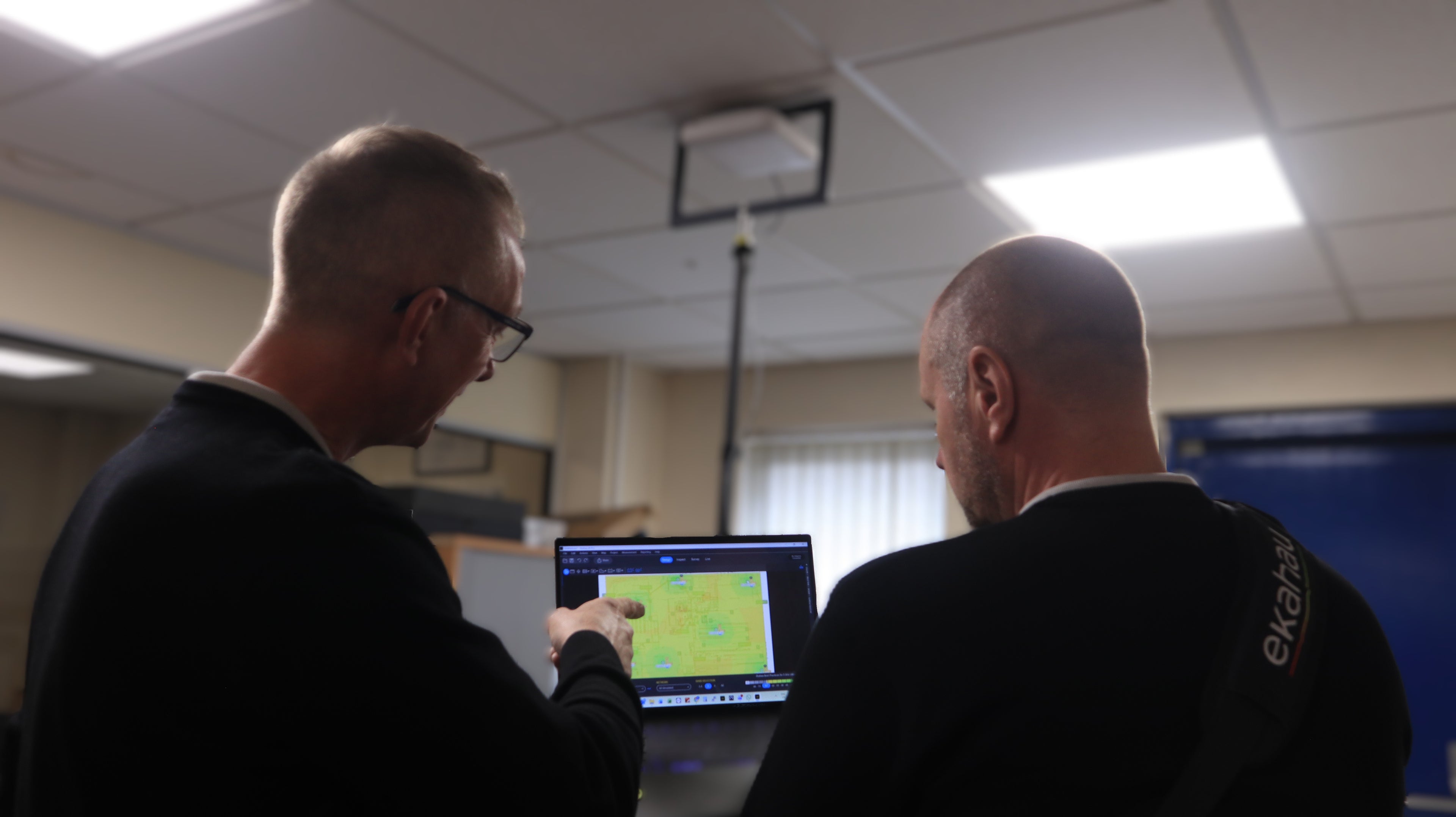 Two men in a room looking at a computer screen with a map displayed.