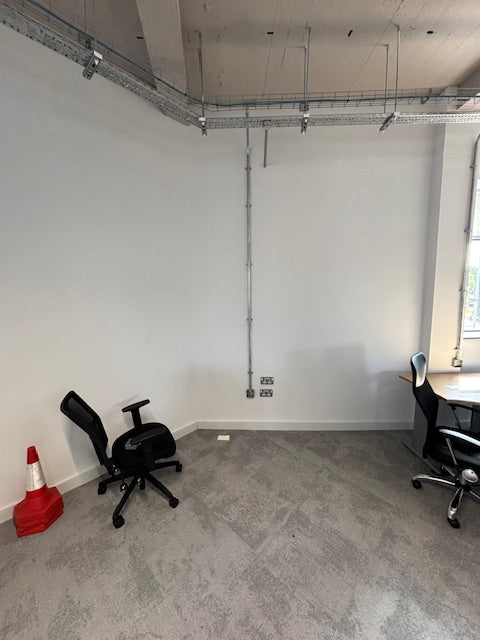 Room with white walls, gray floor, and a red traffic cone.